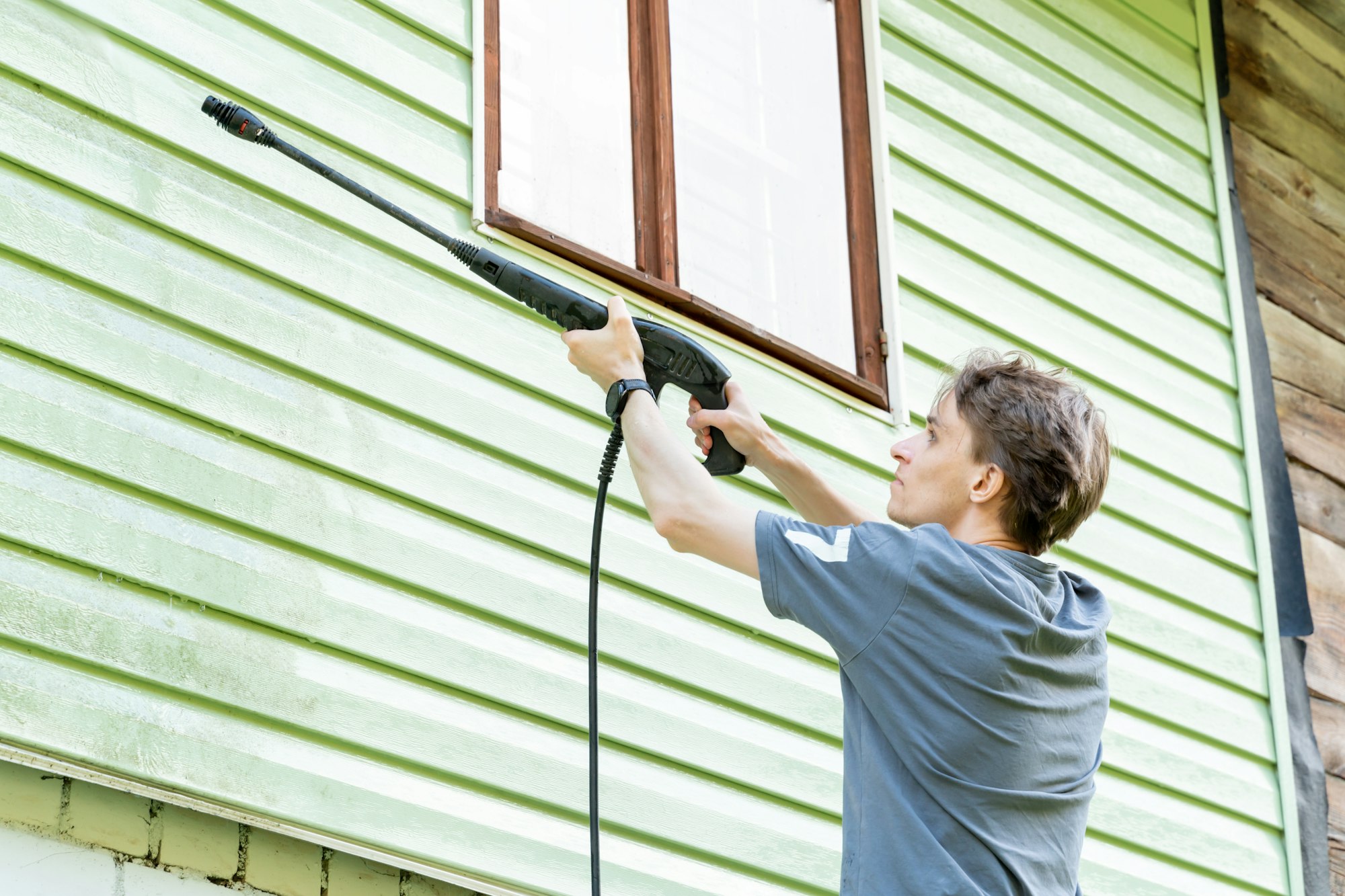 A young man washes the facade of a country house with a high pressure washer