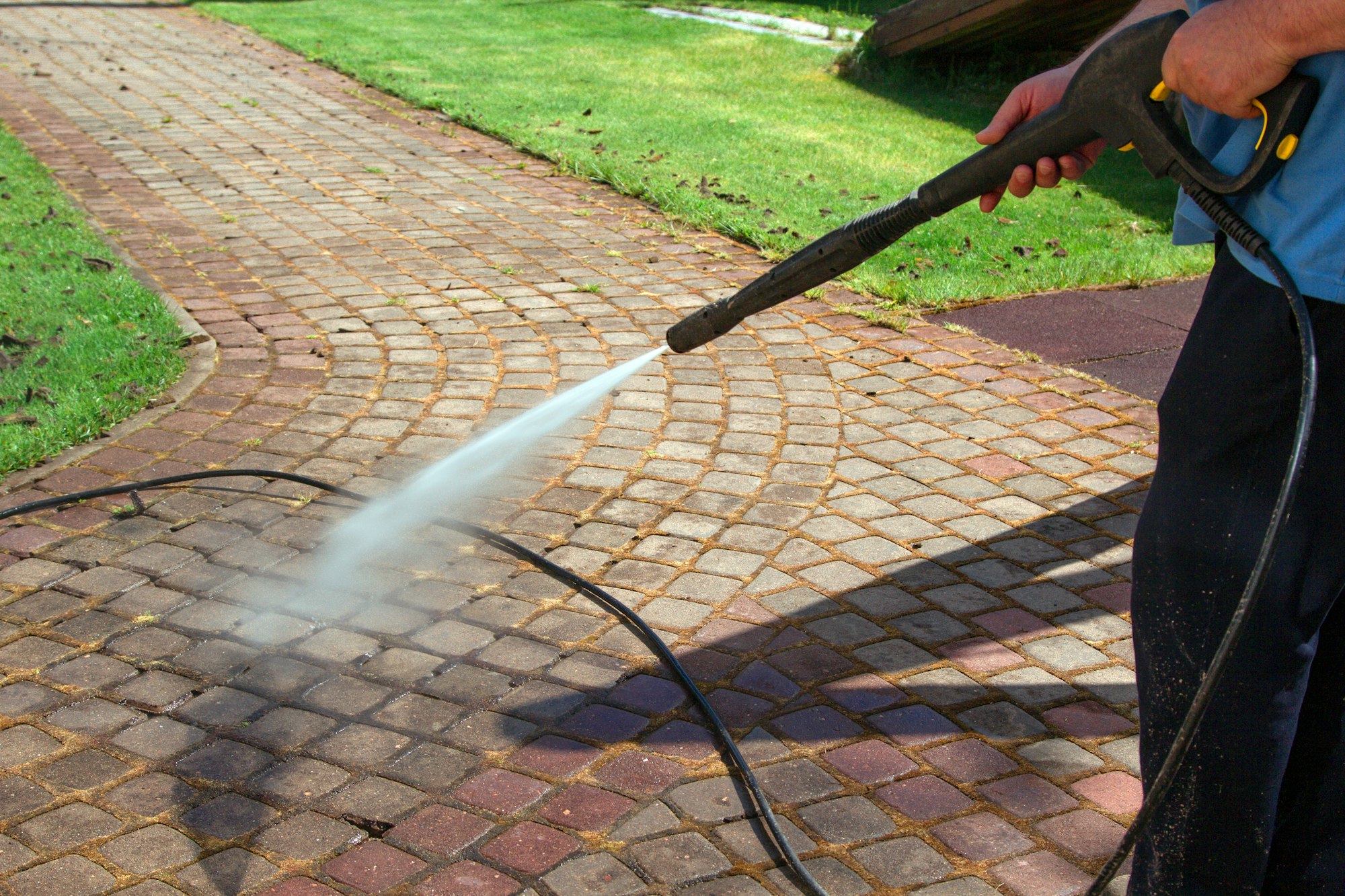 Cleaning street with high pressure power washer, washing stone garden paths