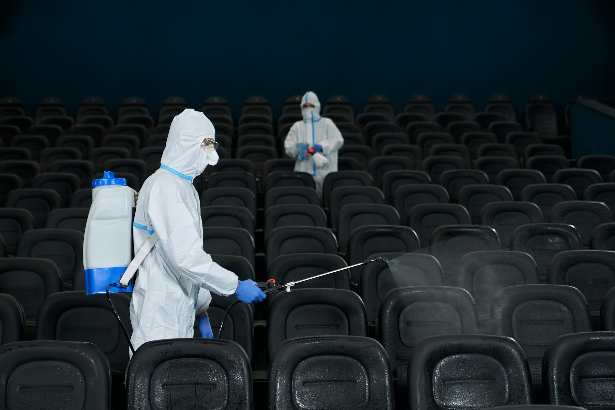 Workers cleaning cinema hall with special disinfectants